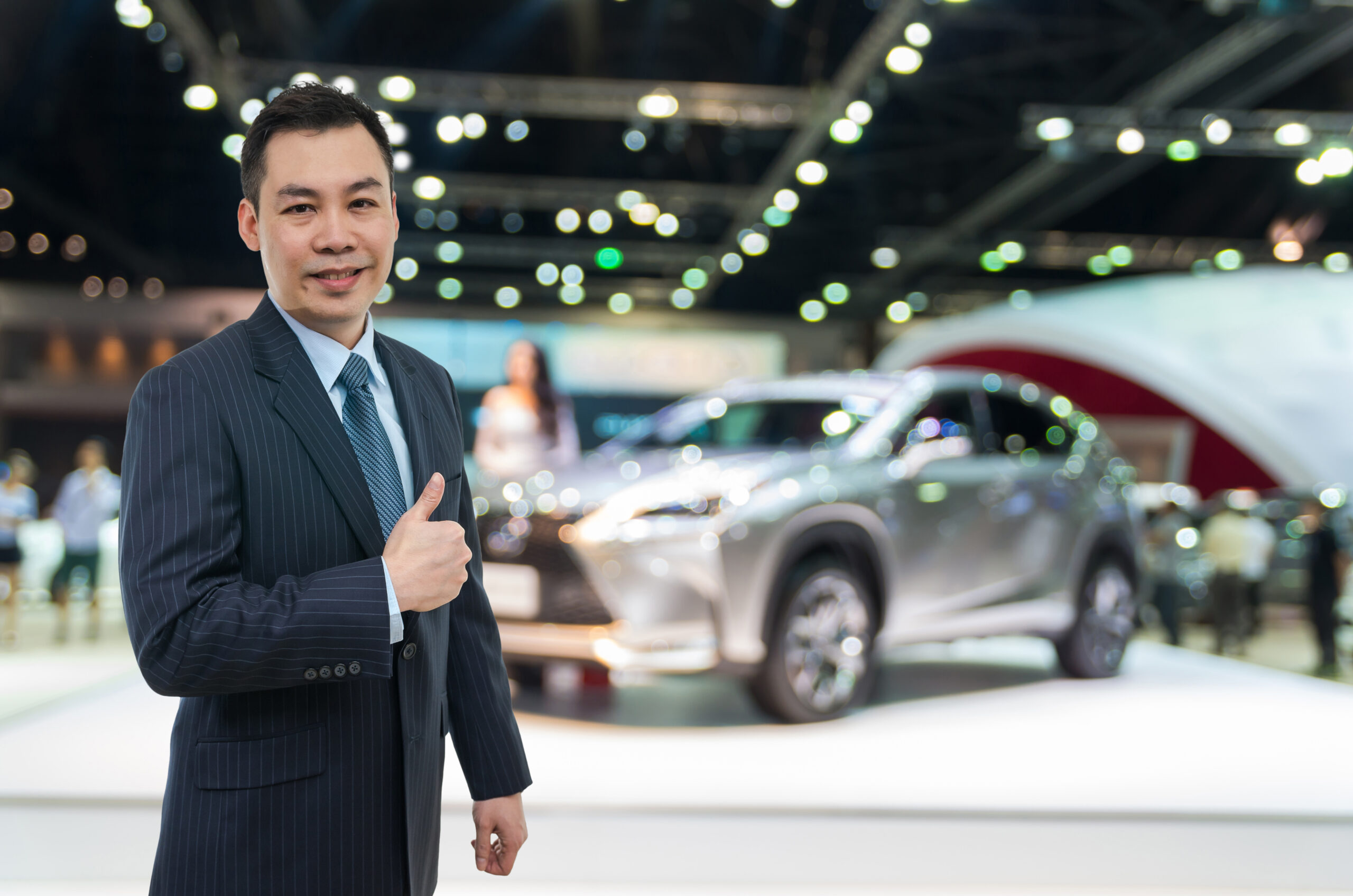 happy-car-salesman-on-auto-show-blurred-background-2024-02-23-05-04-34-utc